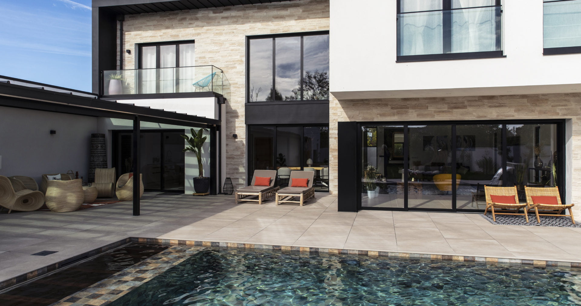 Maison moderne avec habillage en revêtement de plaque de parement Portland ton naturel de chez ORSOL donnant sur une terrasse extérieure bordant une piscine creusée