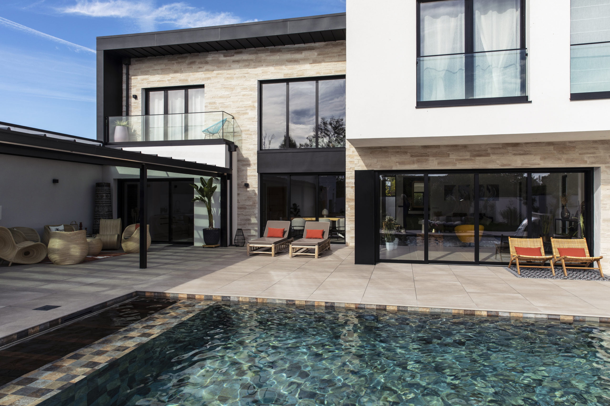 Maison moderne avec habillage en revêtement de plaque de parement Portland ton naturel de chez ORSOL donnant sur une terrasse extérieure bordant une piscine creusée