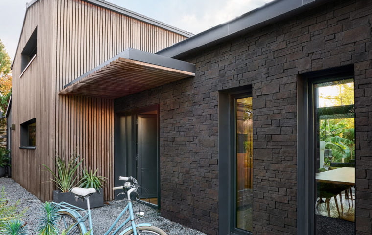 Façade de maison extérieure, d'un côté recouverte d'un revêtement en bois et de l'autre recouvert de parement Cubik ton anthracite de chez ORSOL