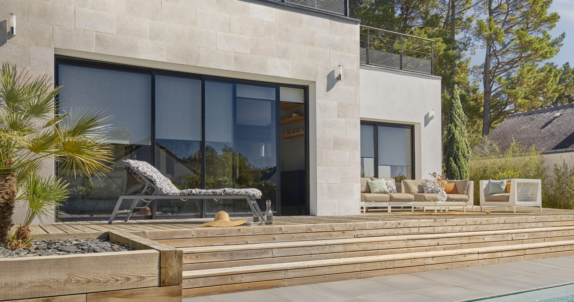 Façade extérieure habillée en parement Brécy face à une terrasse en bois avec des escaliers descendant vers piscine creusée