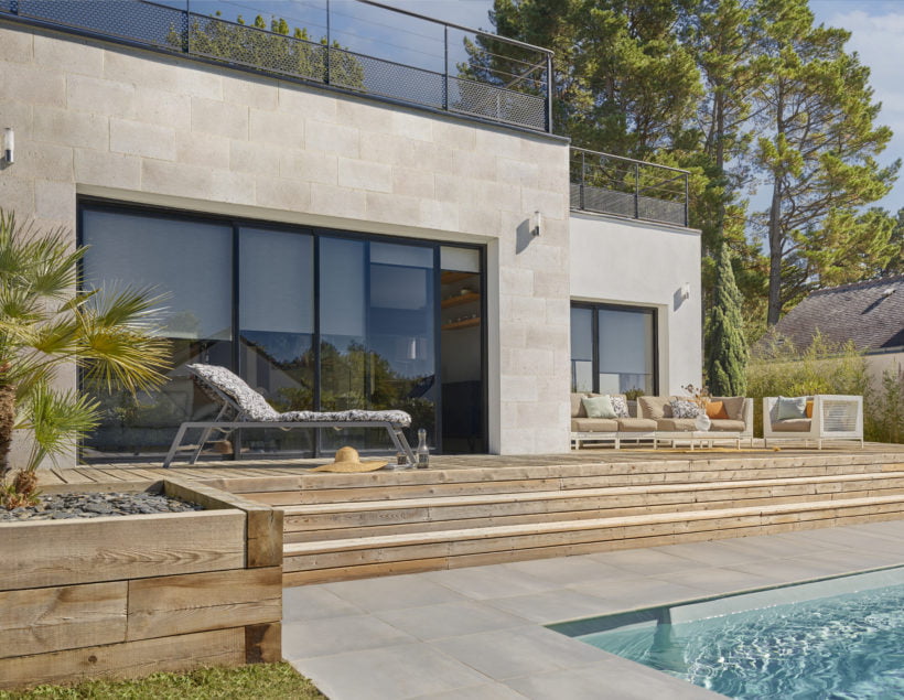 Façade extérieure habillée en parement Brécy face à une terrasse en bois avec des escaliers descendant vers piscine creusée