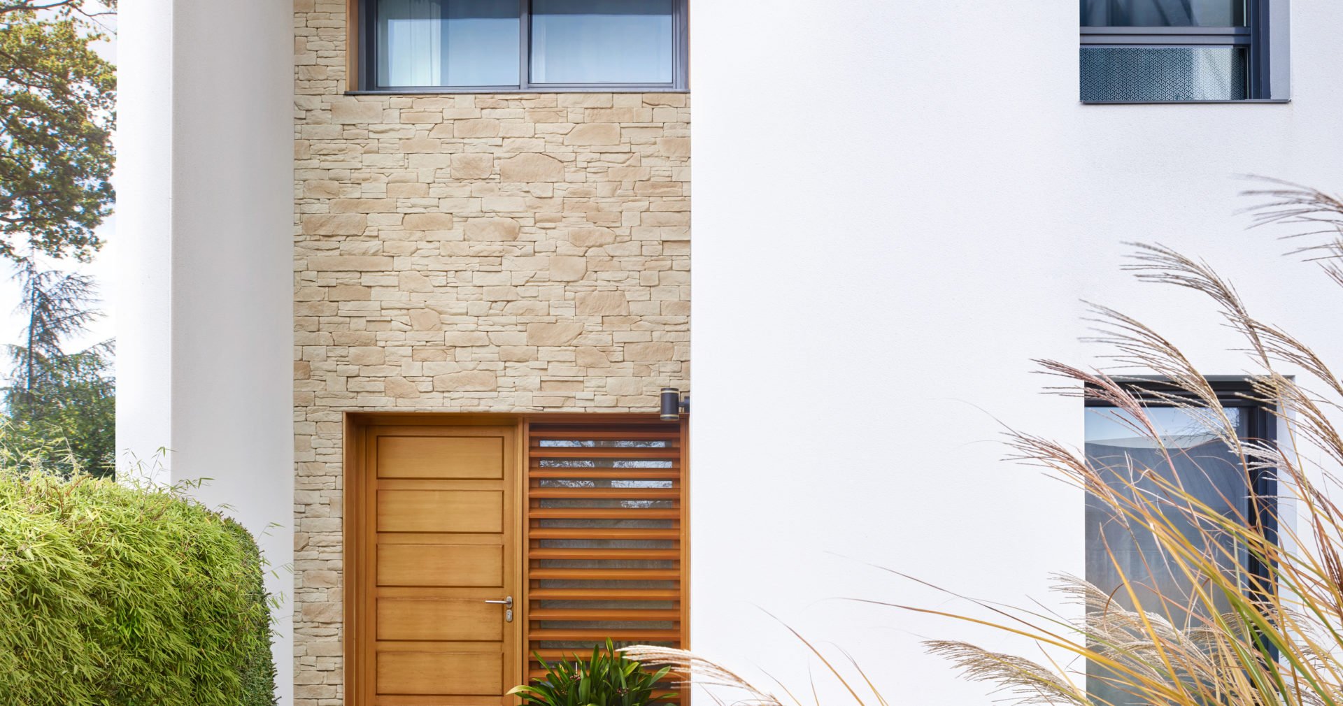 Façade de maison moderne blanche avec entrée abritée recouvert de plaques de parement Tahoe en ton naturel de chez ORSOL