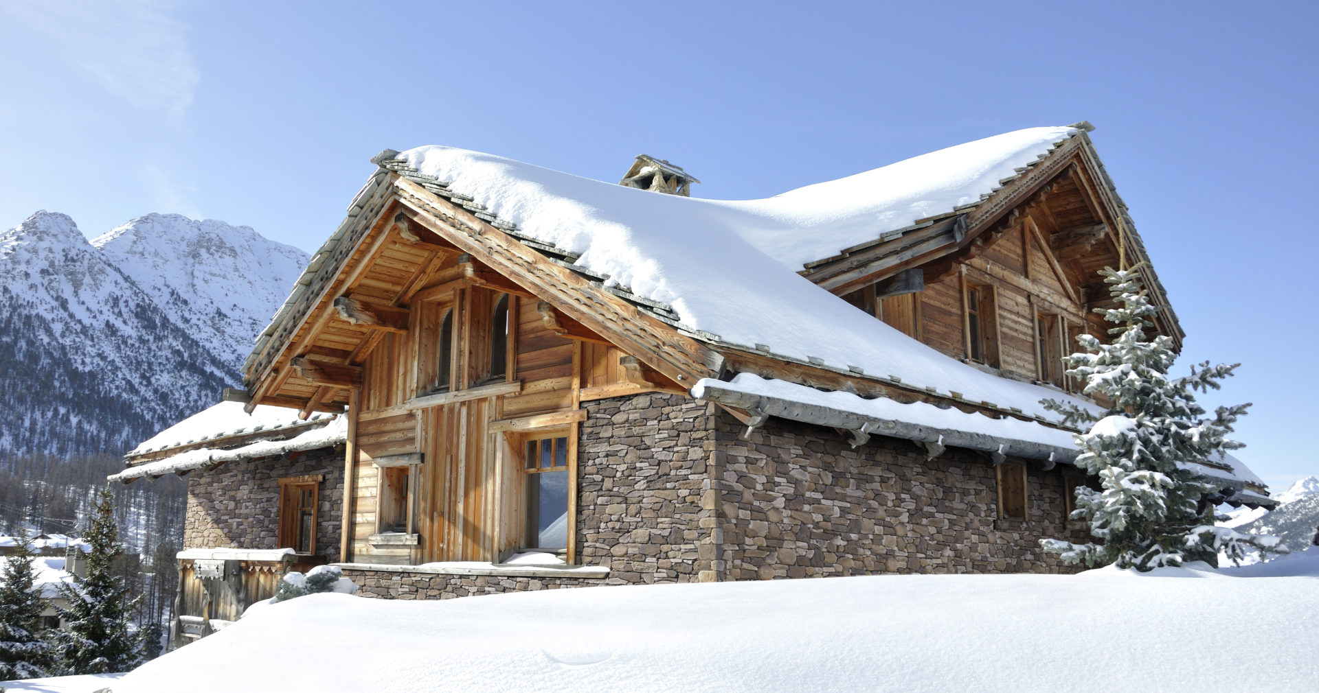 Un chalet de montagne avec parement "Roca" de la marque ORSOL est niché dans un paysage enneigé. Le chalet présente une harmonieuse combinaison de bois naturel et de pierres de parement grises qui lui confèrent un aspect à la fois rustique et élégant.